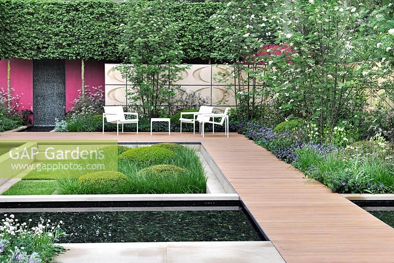 The Brewin Dolphin garden - Wooden boardwalk, pond, furniture, flowering borders with Sorbus aucuparia - rowan trees and sunken garden with box balls and ornamental grass 