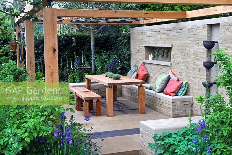 Outdoor seating and dining area with open pergola, wooden table and wall mounted water feature