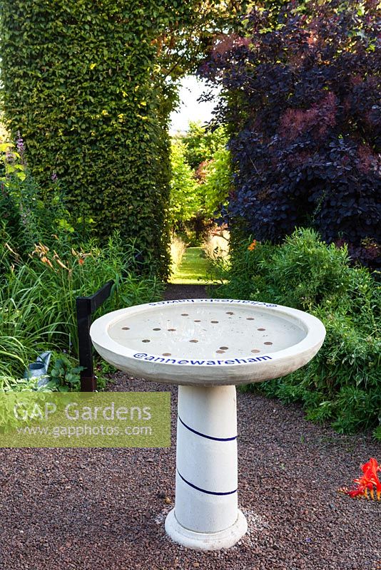 Birdbath inscribed with Twitter names of Anne Wareham and Charles Hawes in their Front Garden. View to tunnel of Carpinus betulus (Hornbeam). Cotinus coggygria 'Grace'. Veddw House Garden, Monmouthshire, Wales