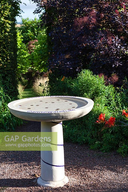 Birdbath inscribed with Twitter names of Anne Wareham and Charles Hawes in their Front Garden. View to tunnel of Carpinus betulus (Hornbeam). Cotinus coggygria 'Grace'. Veddw House Garden, Monmouthshire, Wales
