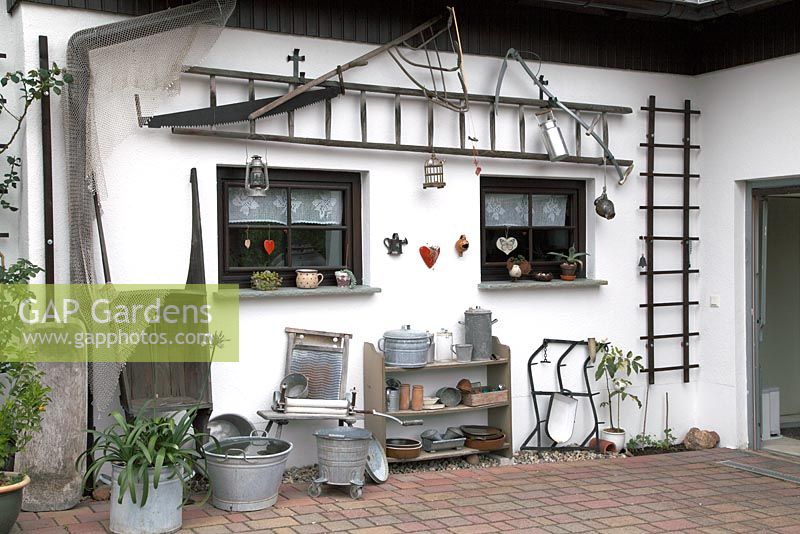 Wall decorated with metal tubs, ladders, washboard, milk jug, scythe, bucket, saw, cart, trough and other decorative objects