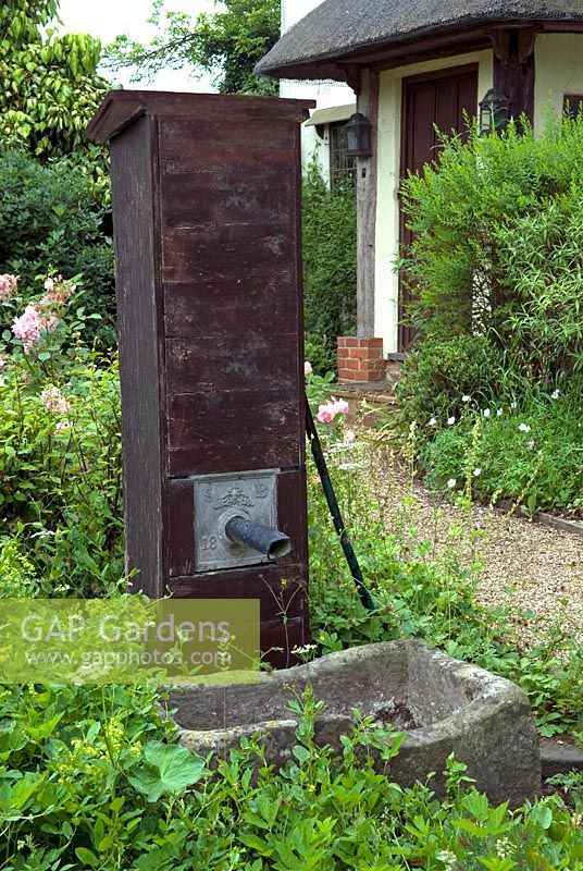Rustic pump and stone container retained as features in cottage garden 