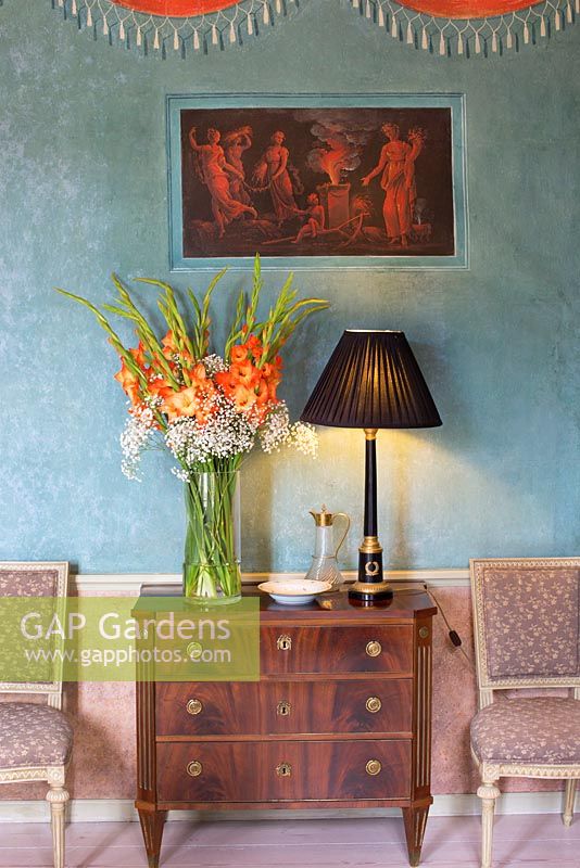 Gladiolus in vase in old house, antique lamp, Chest of Drawers, chairs