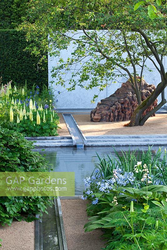 Amalanchier tree, a water rill and pool with a cedar sculpture by Ursula von Rydingsvard surrounded by planting including Lupinus 'Chandelier', Phlox divaricata 'Clouds of Perfume', Euphorbia and Orlaya grandiflora in The Laurent-Perrier Garden, RHS Chelsea Flower Show 2014