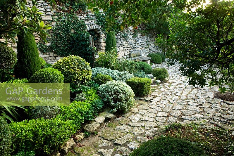 Stone terrace and wall with stone bench and clipped shrubs 