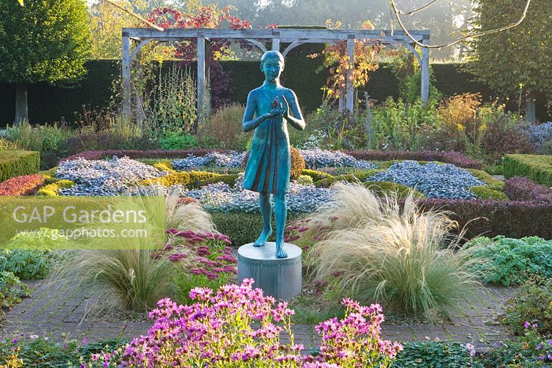The hedged in formal garden at dawn with box and berberis hedging and topiary - girl statue called the 'lamp of wisdom'. Waterperry Gardens, Oxfordshire