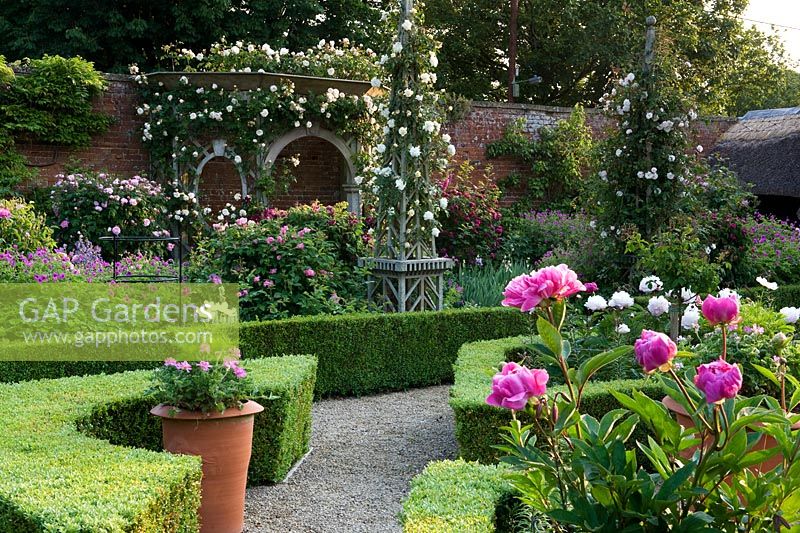 Walled garden with ornate wooden obelisks and arbour. Very floral scene with pink peonies.  Seend, Wiltshire