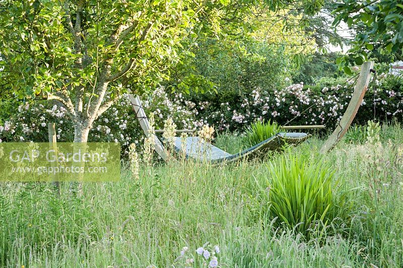 Hammock in the orchard surrounded by long grass, white camassias and meadow cranesbill. Forest Lodge, Pen Selwood, Somerset, UK