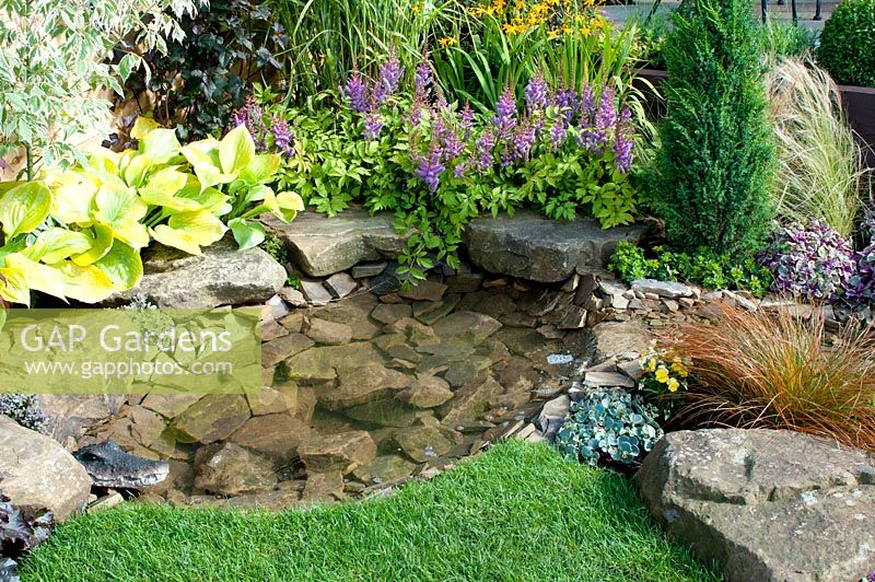 Small garden pool edged by large stones and herbaceous border in the 'Hillside' garden created by Alan Francis Landscapes - Southport Flower Show 2013
 