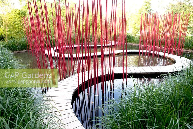 Title: Carre and Rond. Pond and curved walkway decorated with red painted bamboo. Festival des Jardins 2014, Chaumont sur Loire.