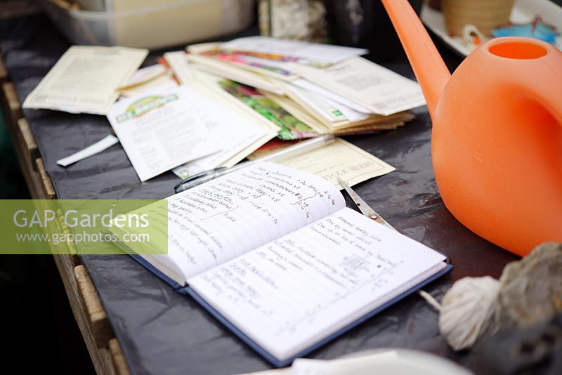 Notebook, Seed packets and watering can on a workbench, Wales, UK.