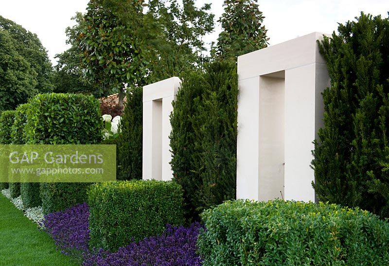 The Just Retirement Garden. Regular topiary shapes of box interspersed with lavender in front of stone wall panels inset with yew hedging. Silver-Gilt medal winner
