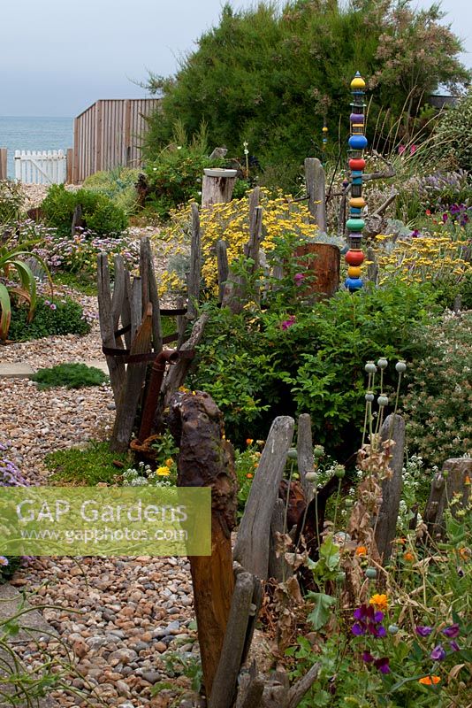 Coastal garden with painted sculpture, drift wood, erigeron, poppies, pebbles and gate to beach