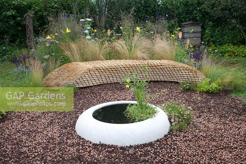 Jordans Wildlife Garden - view of garden seat bench made from straw thatch with mulch of hazelnuts and pine cones with small pond 