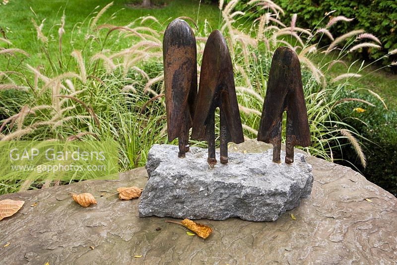 Rusted steel sculptures on a stone table top and Pennisetum setaceum 'Sky Rocket' in backyard garden in autumn. Il Etait Une Fois garden, Otterburn Park, Monteregie, Quebec, Canada. 