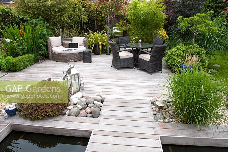 Contemporary Ipe hard wood deck over pond, contrasting texture of rounded pebbles softened by planting of Miscanthus sinensis, Pittosporum 'Tom Thumb'. Euonymus fortunei 'Emerald 'n' Gold' and low Buxus sempervirens hedging