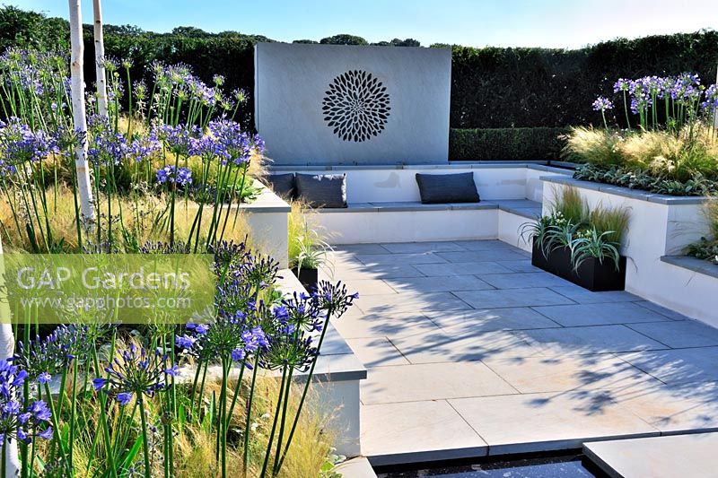 A low maintainance contemporary garden.Raised beds planted with grasses and agapanthus. built in concrete seating. Description: Vogue. Designer: Belinda Belt Sponsor: London Stone Crowder's Nursery