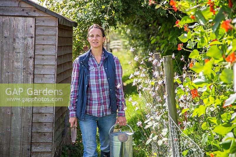 Woman entering allotment carrying watering can and hand trowel