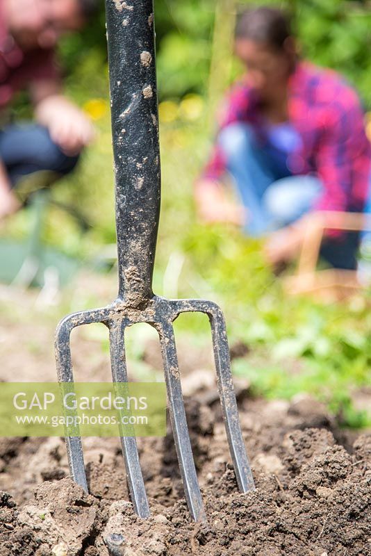 Fork embedded in soil, man and woman working in background