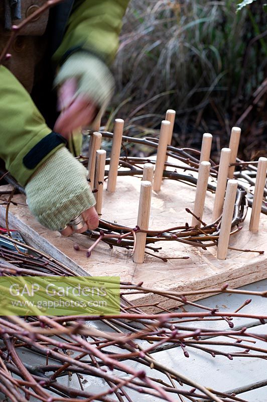Using a peg frame to form the circular base of a wreath out of long twigs 