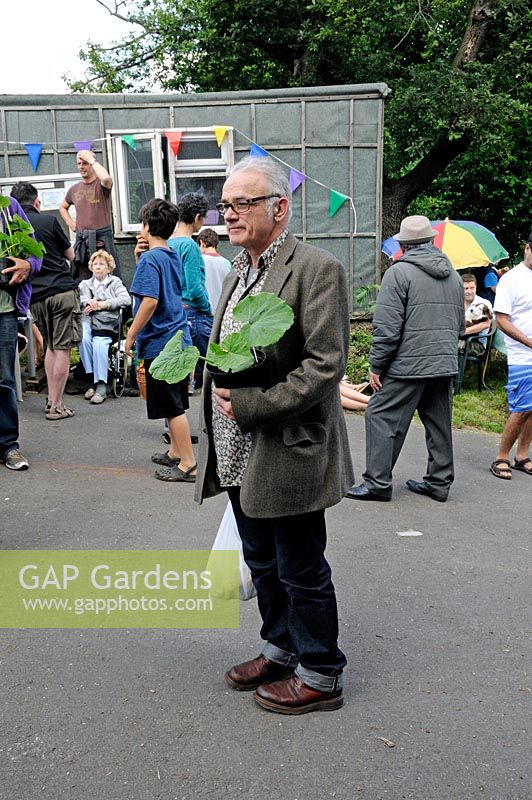 Man holding a courgette or pumpkin plant he has bought at the Alexandra Palace Allotments plant sale, London Borough of Haringey
