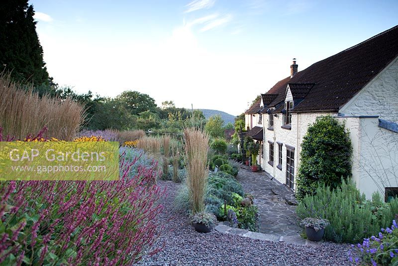 Blue sky over late summer garden planted over terraces with gravel paths and a stone cottage