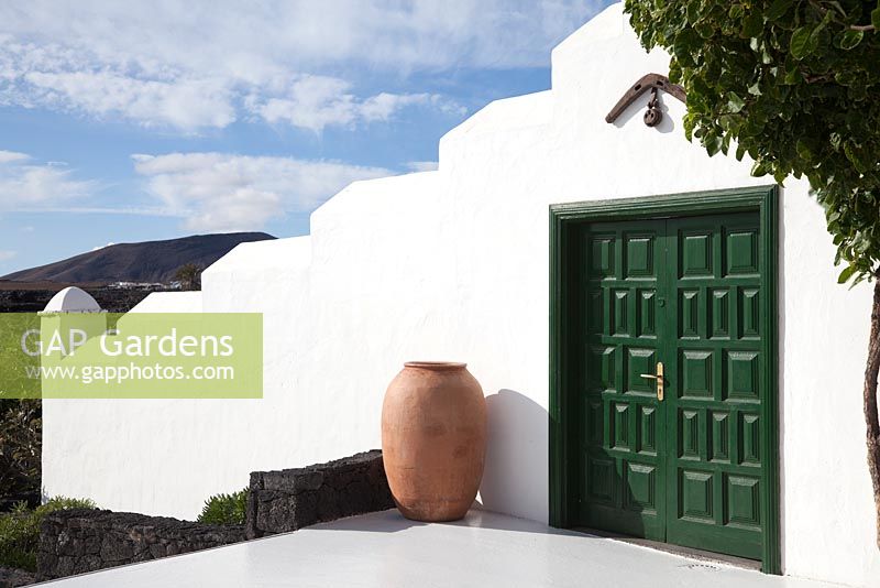 Large pithoi against white washed wall and green door with view of volcano beyond 