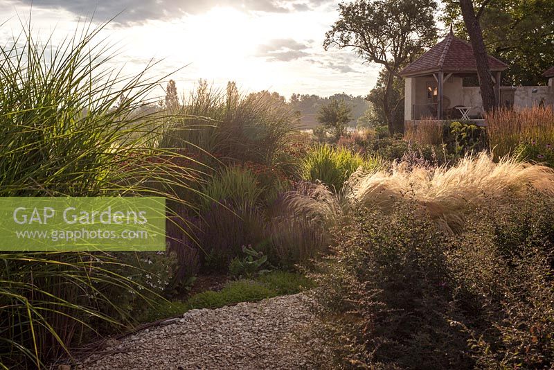 Gravel path leading through naturalistic Dutch style planting with Miscanthus, Nasella, perennials with pavilion in the background