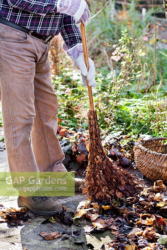 Man sweeping up autumn leaves on patio using home made birch broom.