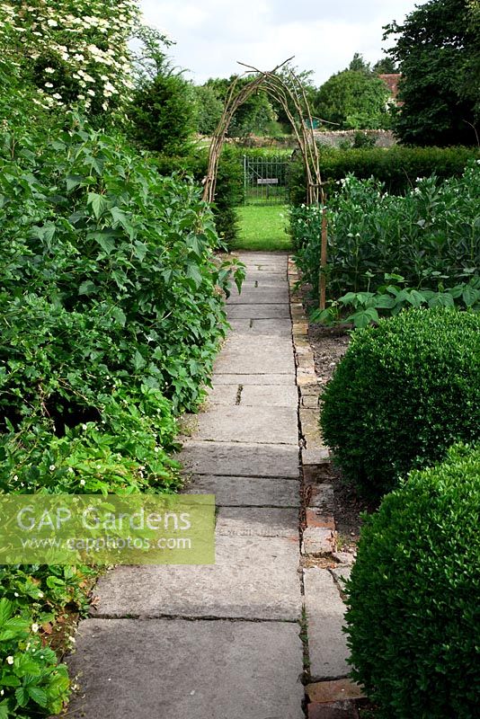 Stone pathway through fruit and vegetable garden with buxus balls - box and coppiced wood archway