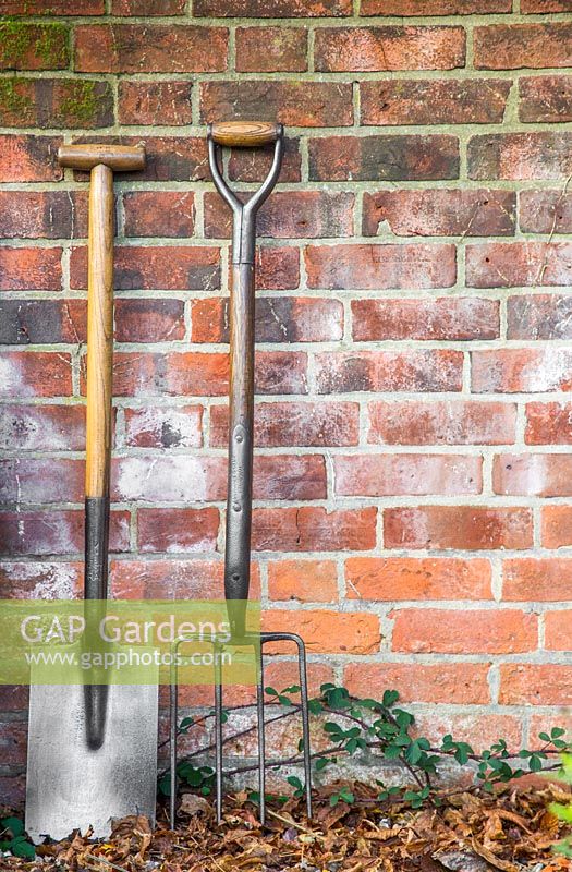 Vintage wooden fork and spade against a brick wall