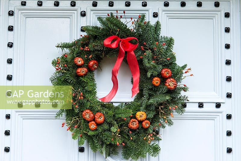 Lovely old front door is decorated with a  traditional, long lasting Christmas wreath made using spruce, with red rose hips, dried pumpkins and ribbon. 