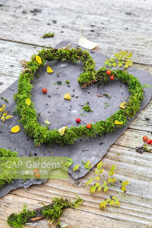 Christmas heart decorations made from moss, on slate against a wooden backdrop. 