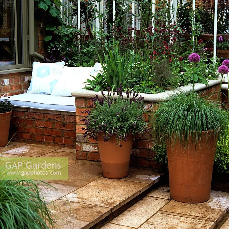 Raised flower bed doubles as side to brick seat with cushions, built in sunny position by conservatory.