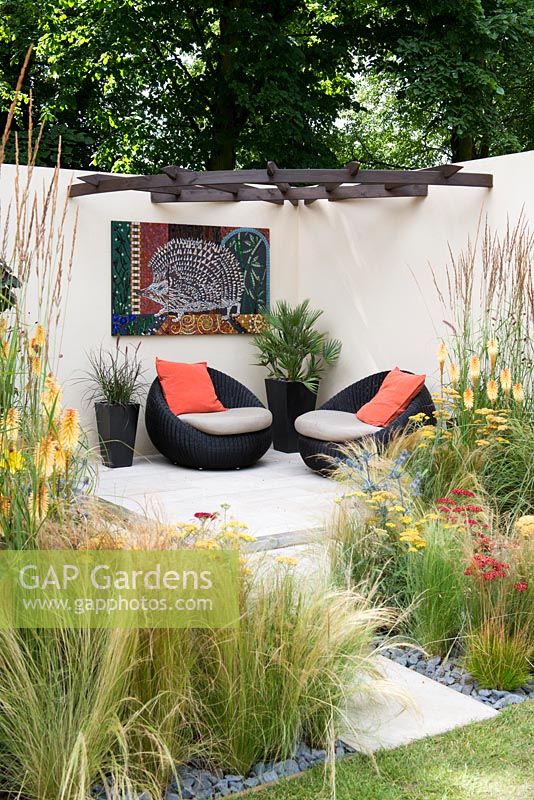 A contemporary courtyard garden with seating area, surrounded with Stipa and Calamagrostis grasses with Achillea, Kniphofia and Eryngium.