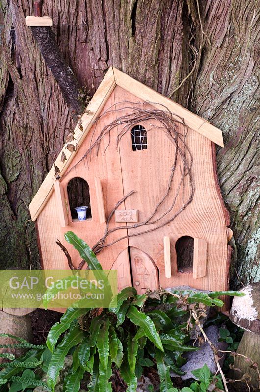 Child's miniature house at the base of a tree with ferns
