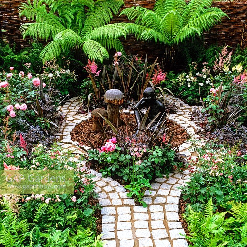 Granite setts laid in shape of a poppy, to encourage childrens interest in plants. Tree ferns, roses, astilbe.