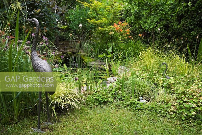 Metal Heron bird sculptures next to pond in backyard garden in summer, Quebec, Canada
