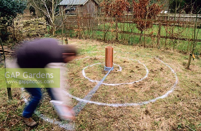 Man tracing spiral on rough grass in autumn with can of marker paint in order to plant a crocus spiral feature for spring