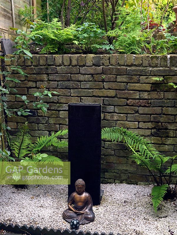 A buddha in front of a modern water feature in a small zen courtyard garden.
