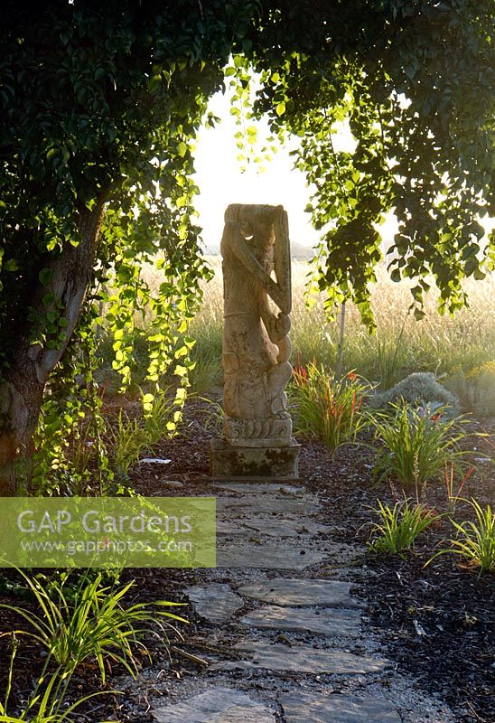 A piece of stone sculpture located at the end of a long stone path. Amongst a bed of newly planted mixed grasses. Domaine de Cambou, Verfeil, Haute-Garonne, Midi Pyranees, France.
