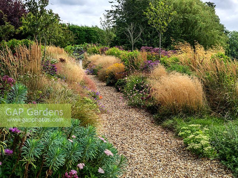 A gravel path lined by double mixed borders planted with perennials and grasses. Planting includes Euphorbia, Achillea, Sedum, Eupatorium, Monarda, Guara and Rudbeckia with Stipa and Calamagrostis grasses.