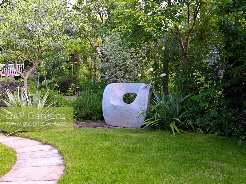 Overlooking lawn, sculptural moulded concrete chair, dogwood behind and clumps of Astelia chathamica to each side.