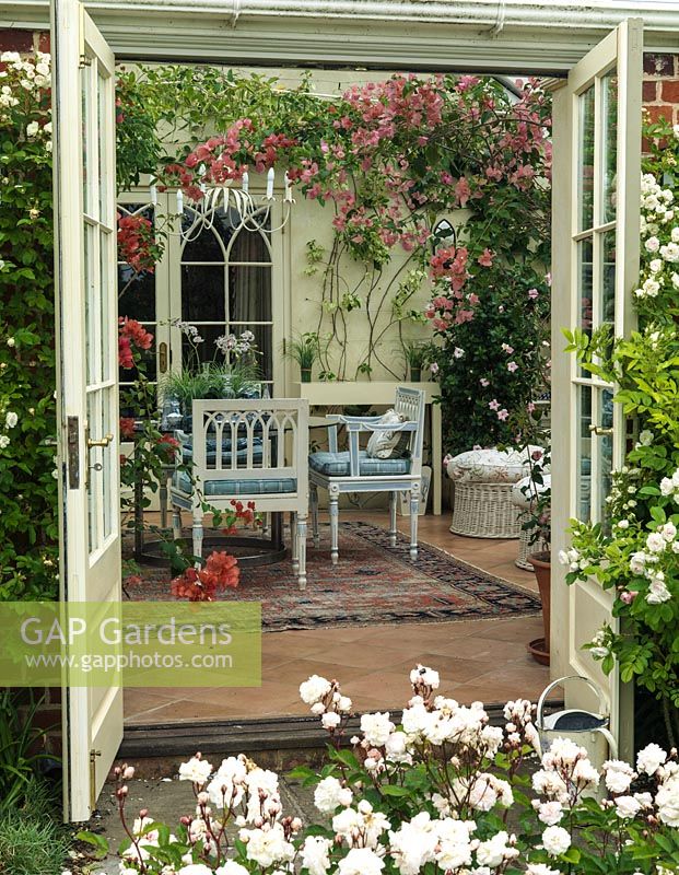 Seen from rose filled courtyard, conservatory with pink and white bougainvillea trained up the wall above seating area