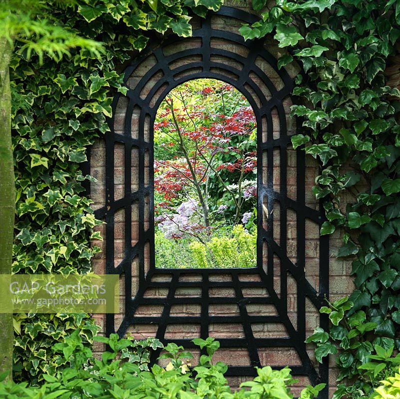 A mirror trompe l'oeil creates a focal point on a garden wall. Made from mirror from local hardware store, the surround from reclaimed batoning.