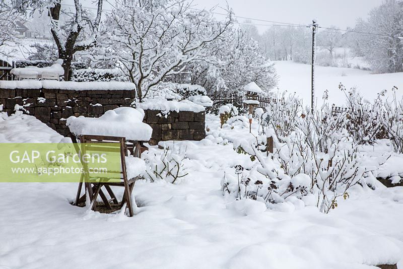 Winter scene with stone walls, garden furniture and shrubs