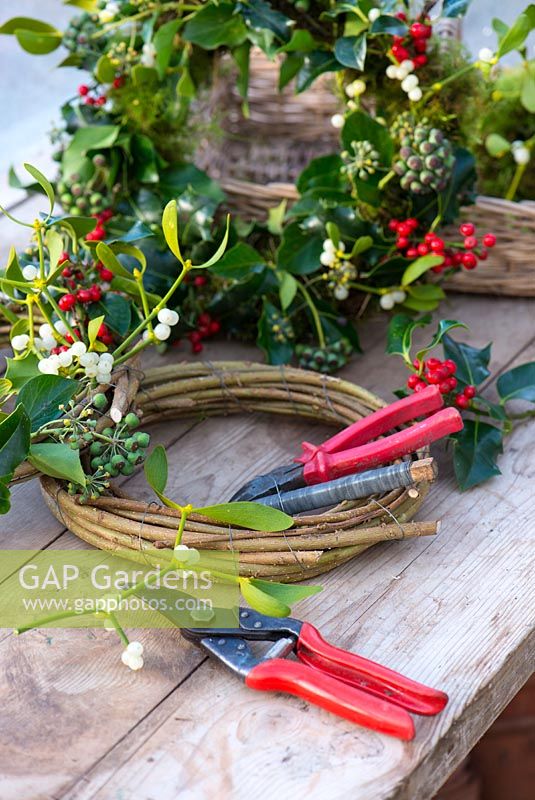 Materials and tools for making a Christmas wreath from natural materials. Ivy, mistletoe and crab apples.