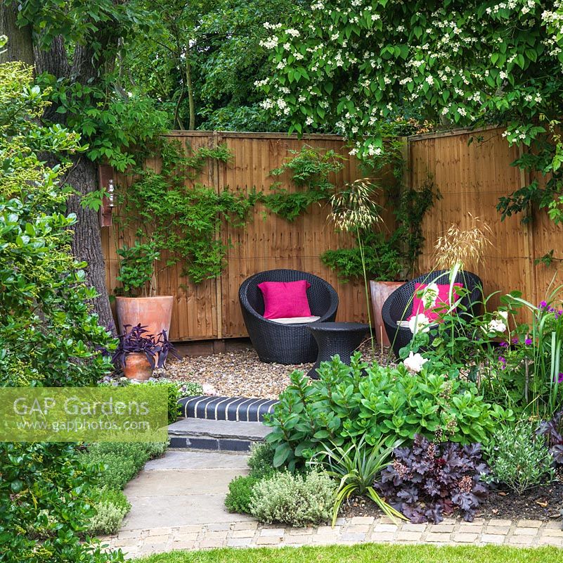 A sheltered seating area with contemporary garden furniture is raised in the corner of a modern garden.