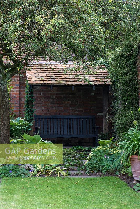 A tiled roof arbor built against a wall shelters a garden bench.