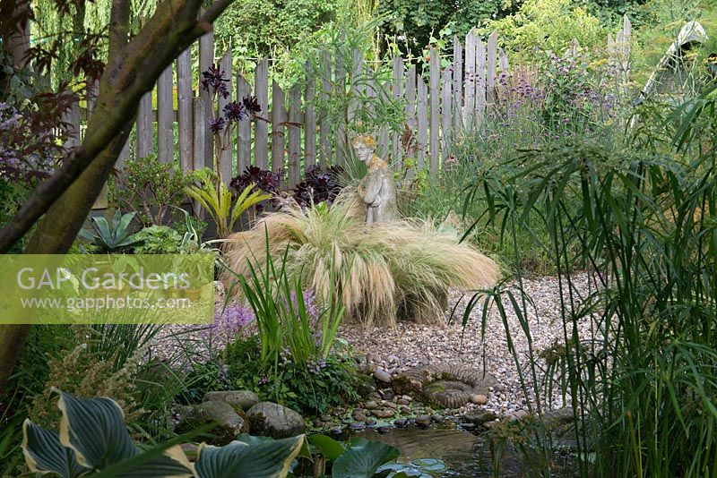 A gravel garden with Stipa grasses surrounding a stone statue.